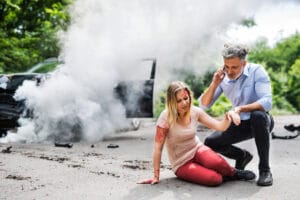 Young woman by the car after an accident and a man making a phone call.